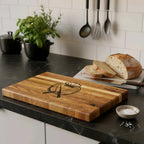 Wooden cutting board with pumpkin and knife design on a kitchen counter with bread and salt.