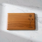 Wooden cutting board with floral design and 'WOODIALE' branding on a marble surface