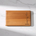 Wooden cutting board with engraved design and 'WOODIE' branding on a marble surface