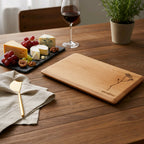 Wooden cutting board with engraved design on a wooden table with cheese platter and wine glass.