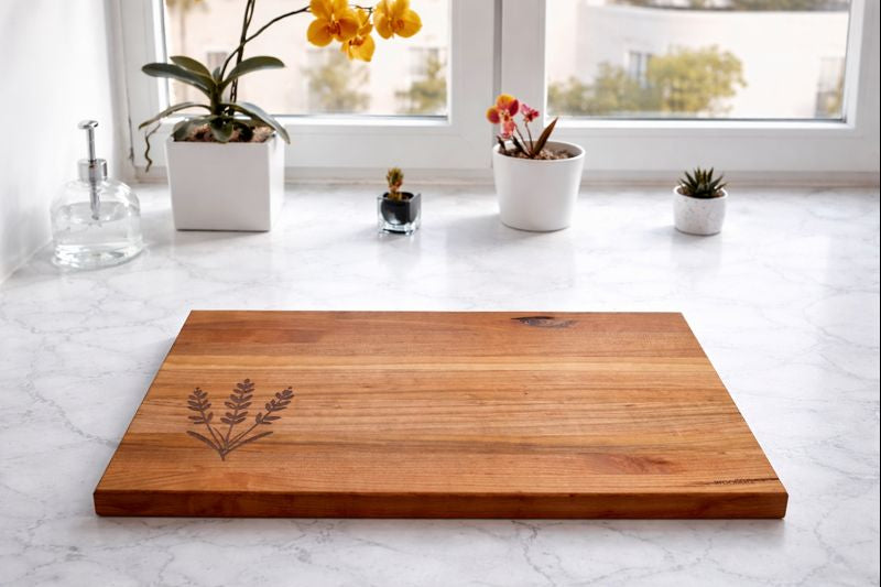 Wooden cutting board with engraved design on a marble countertop with decorative plants.