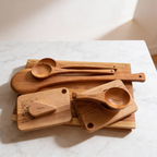 Set of wooden kitchen utensils including cutting boards, spatulas, and ladles on a marble surface.