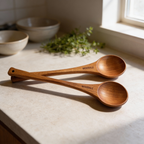 Two wooden spoons on a kitchen counter with bowls and greenery in the background.