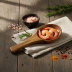 Wooden spoon with shrimps on a wooden surface with spices and herbs.